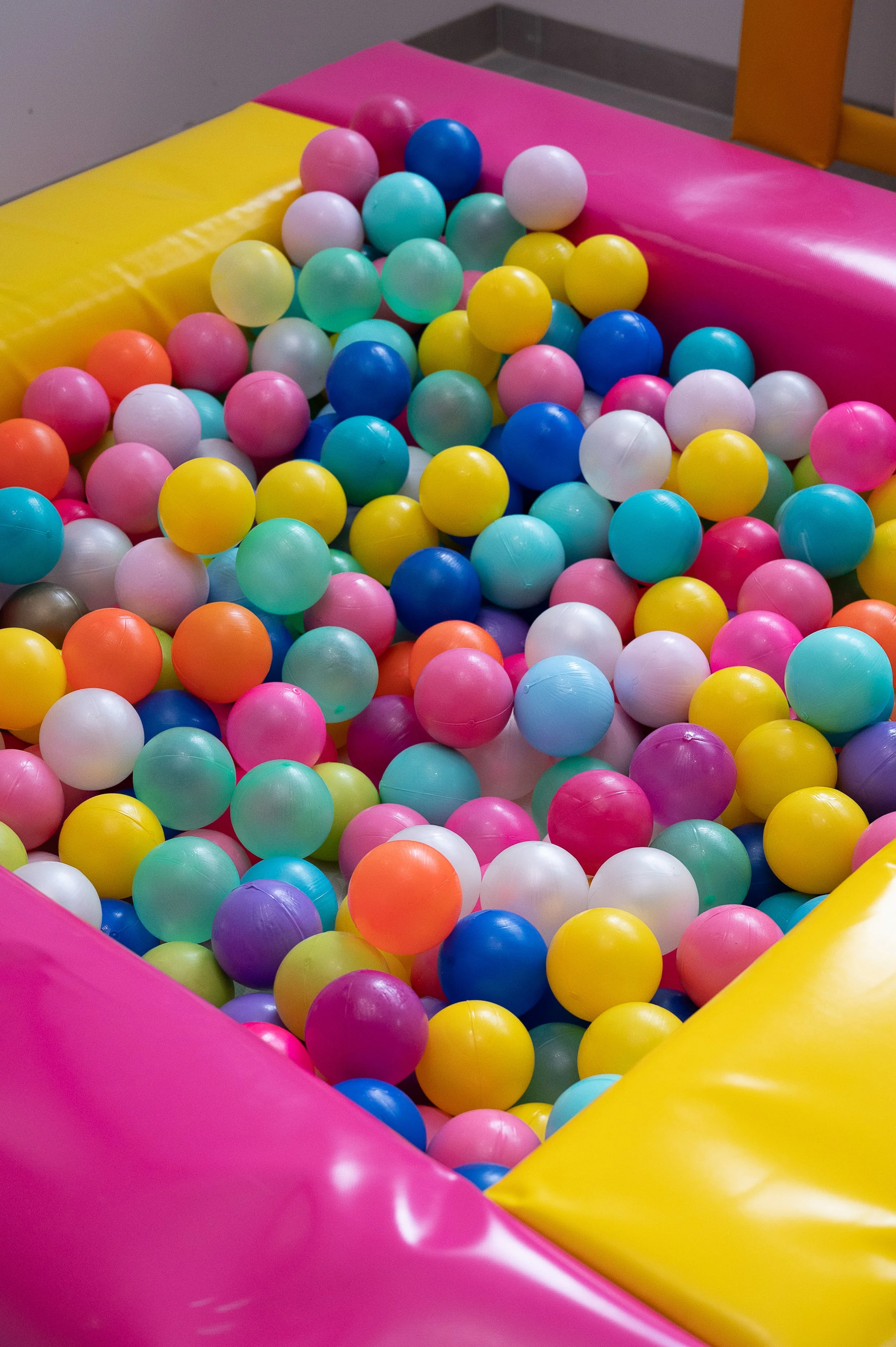 Colorful plastic balls in a ball pit with pink, yellow, and gray padded sides.
