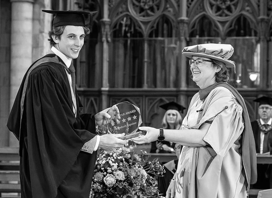 A young man in a graduation cap and gown receiving an award from a woman in academic regalia inside a church or cathedral.