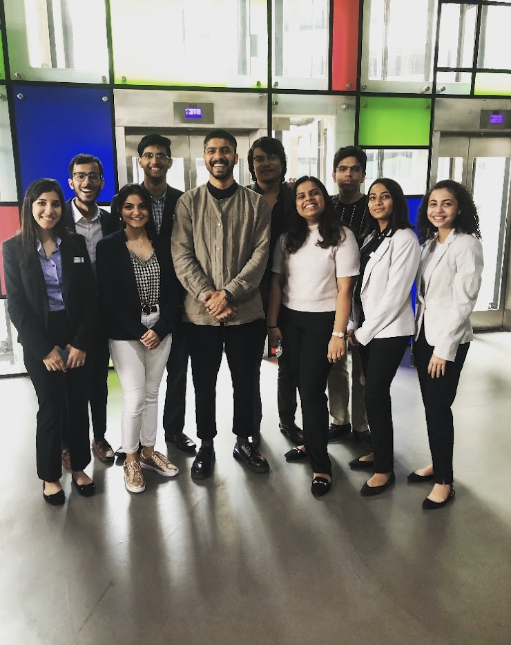 Group of ten diverse young professionals smiling and posing together indoors with colorful panels and glass windows in the background.