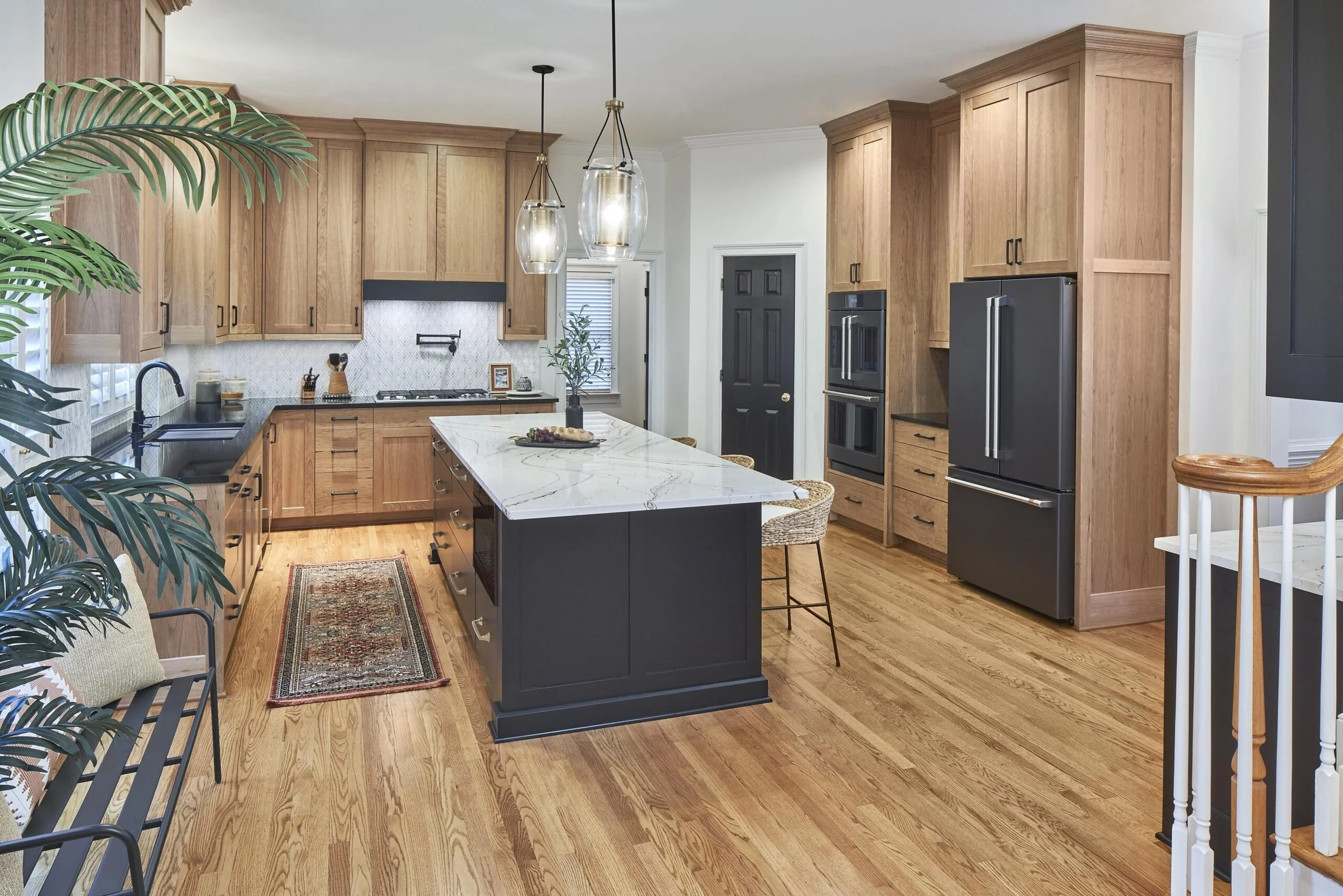 Modern kitchen with wood cabinets, black appliances, marble island, pendant lighting, and hardwood floors.