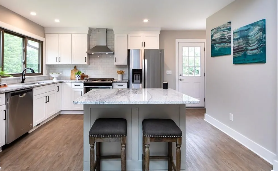 Modern kitchen with white cabinets, stainless steel appliances, a marble island, and blue abstract wall art.