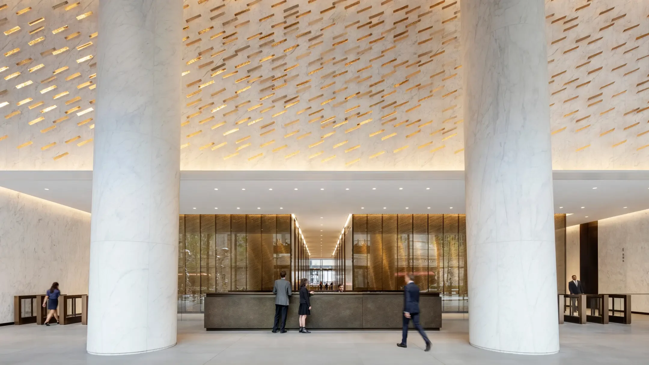 Modern hotel or office lobby with large white marble columns, a reception desk with staff, and decorative ceiling lights.