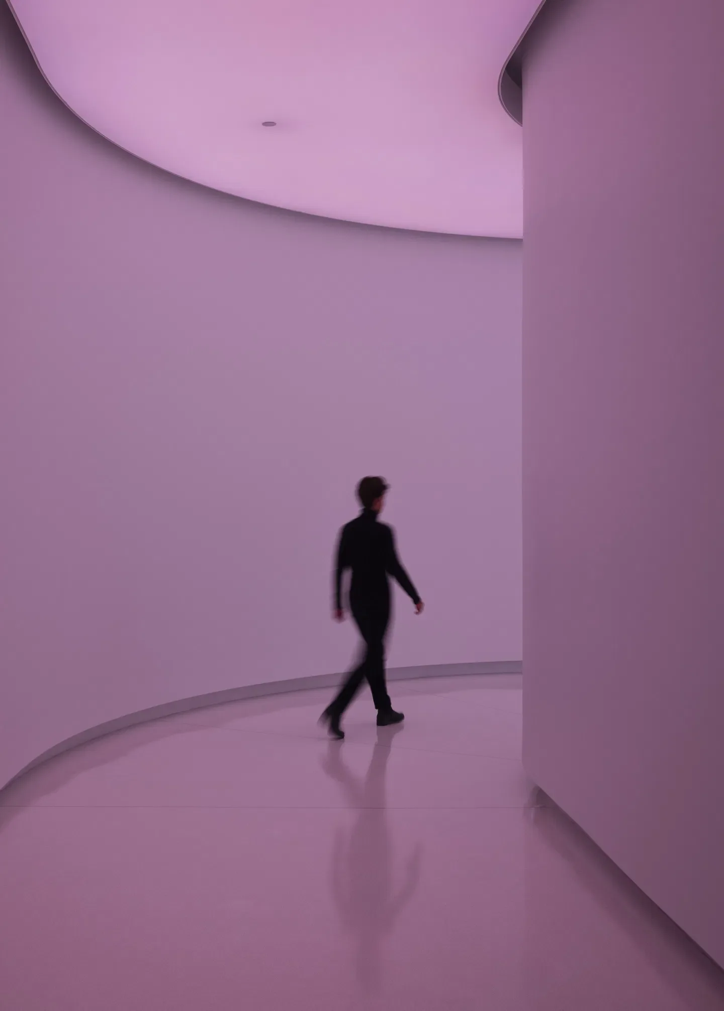 A person walking through a modern, minimalistic hallway with pink lighting and curved walls.