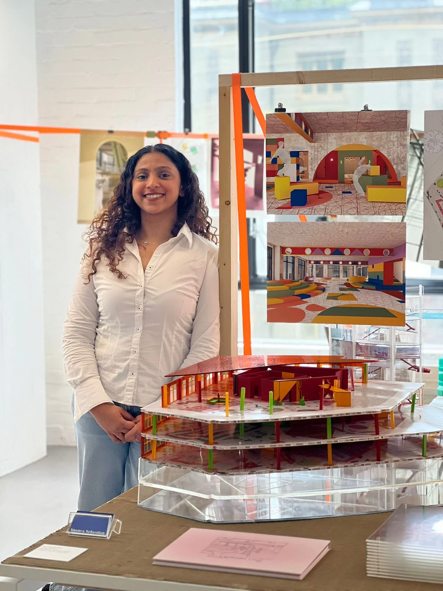 Ananya Sebastian standing next to her thesis project models and drawings displayed at RCA Interior Design Show.