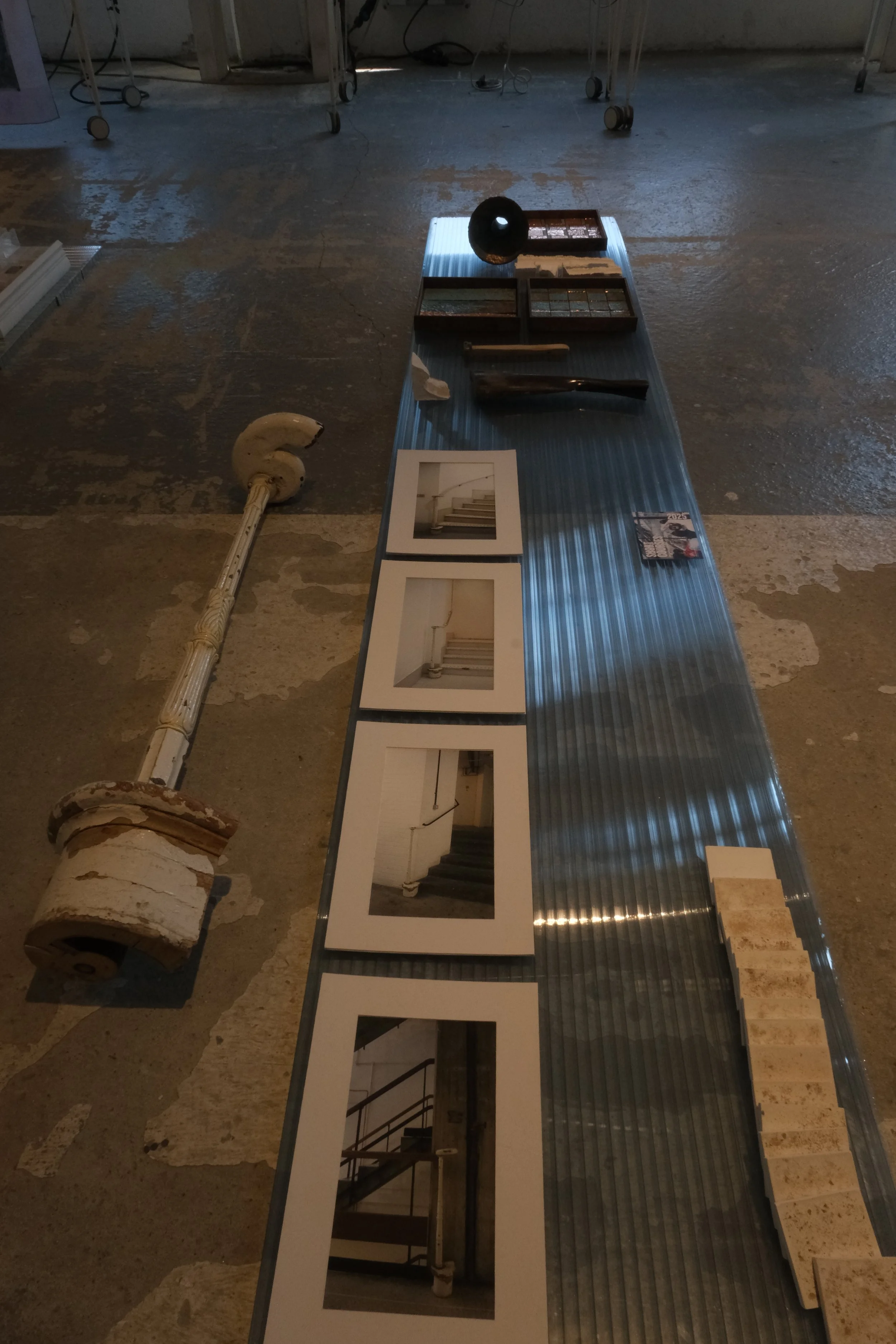 Milan Design Week  and photographs of staircases on a metal tabletop, surrounded by supply boxes and machinery.