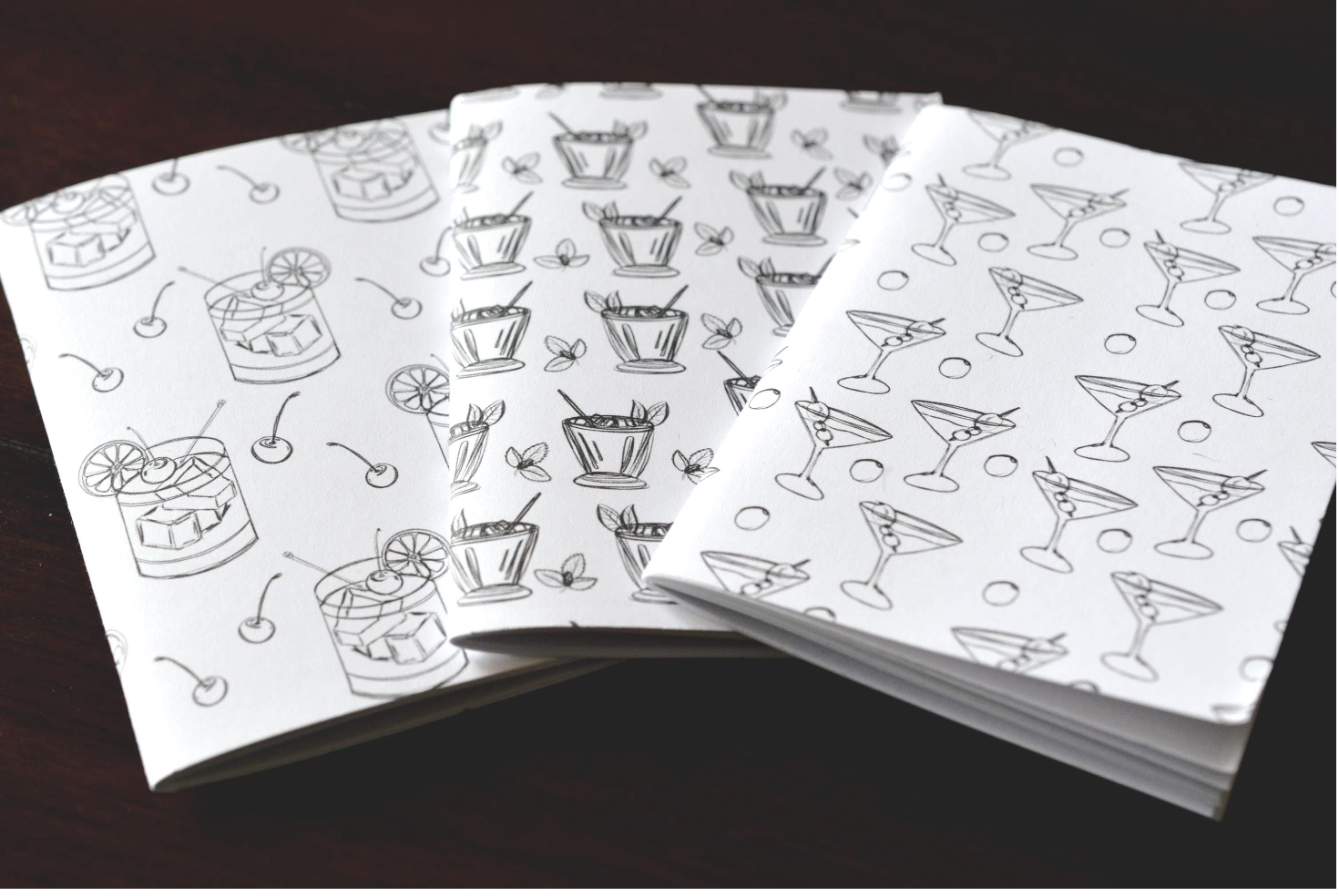 Sheets of paper with printed black and white line drawings of cocktails, including margaritas, martinis, and drinks with cherries and lemon slices.