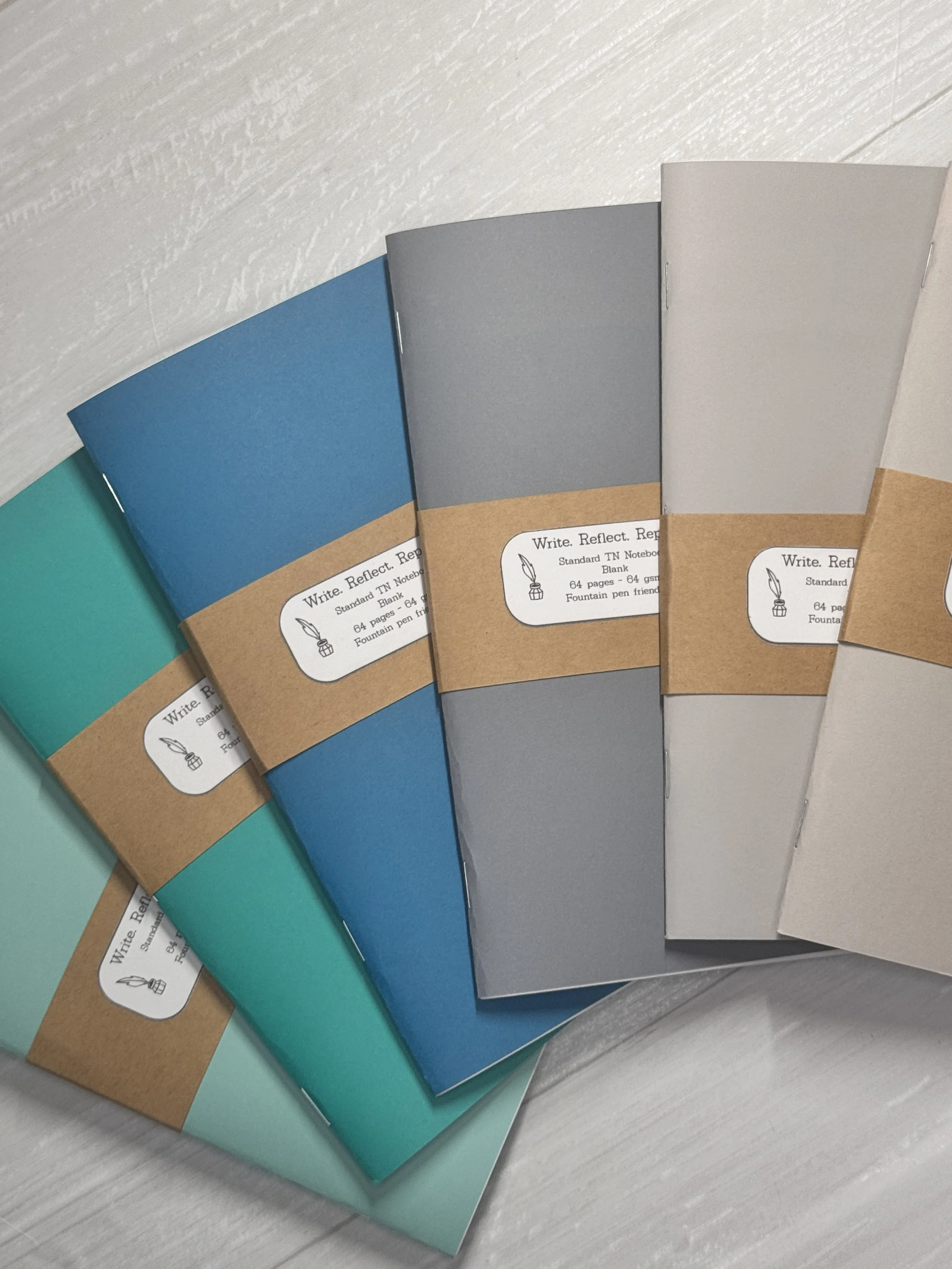 Several notebooks in various colors, including teal, blue, gray, and beige, with brown paper bands around them and white labels on the bands.