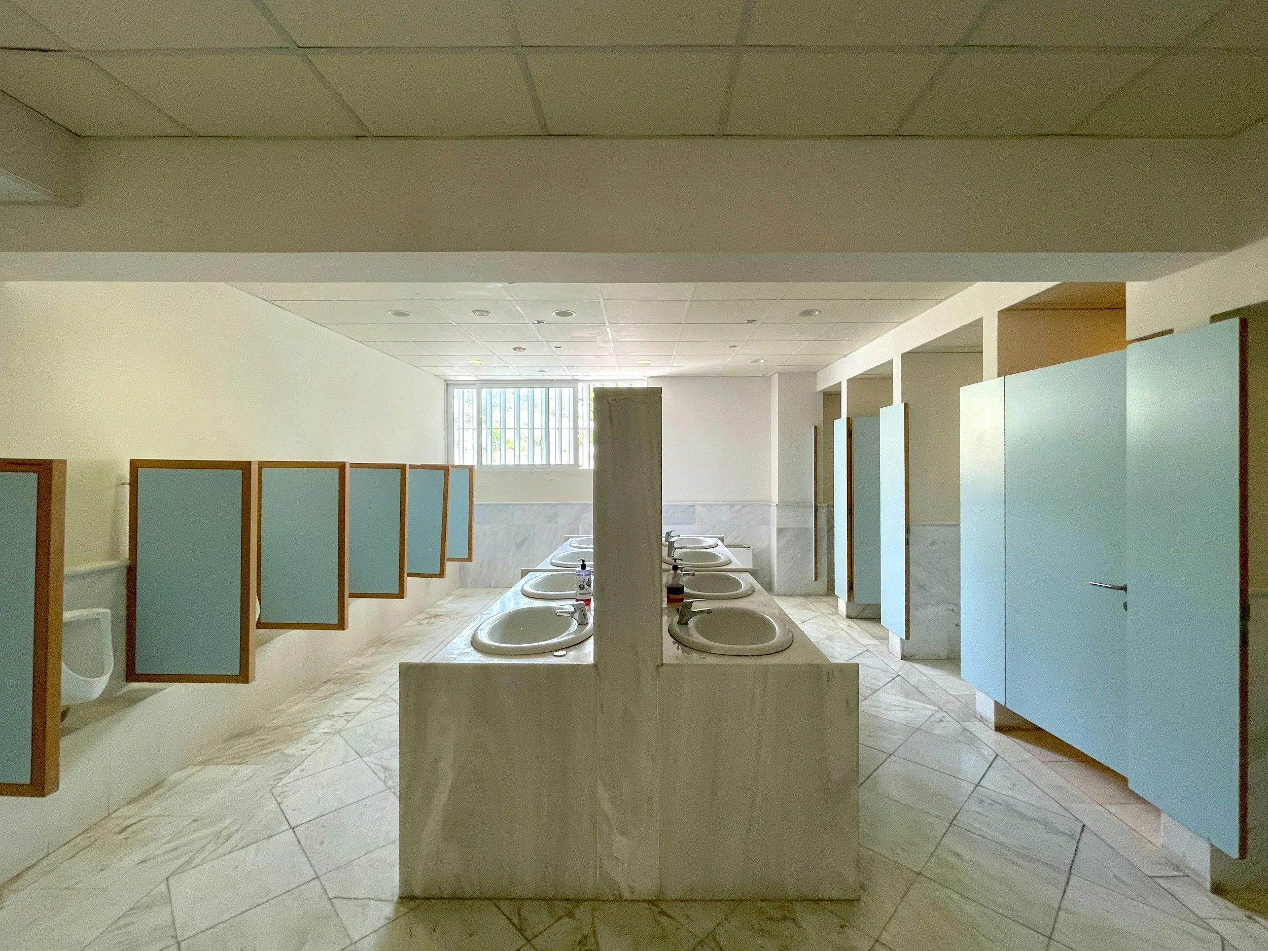 Empty public restroom with multiple sinks and blue stall doors.