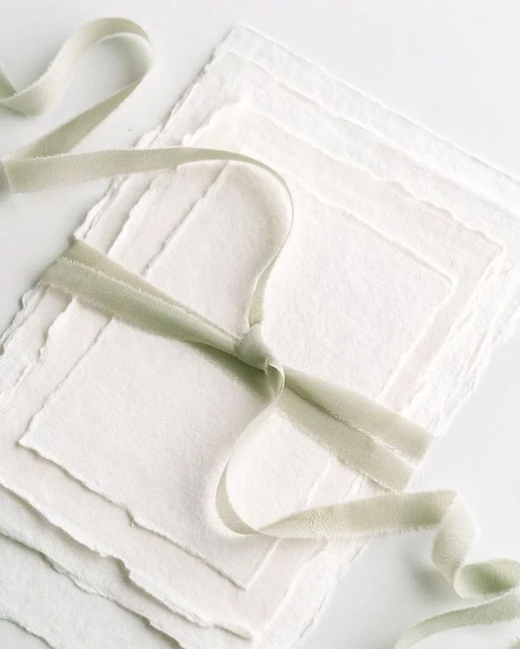 Close-up of white fabric with cut-out lace patterns, tied with a cream-colored ribbon.