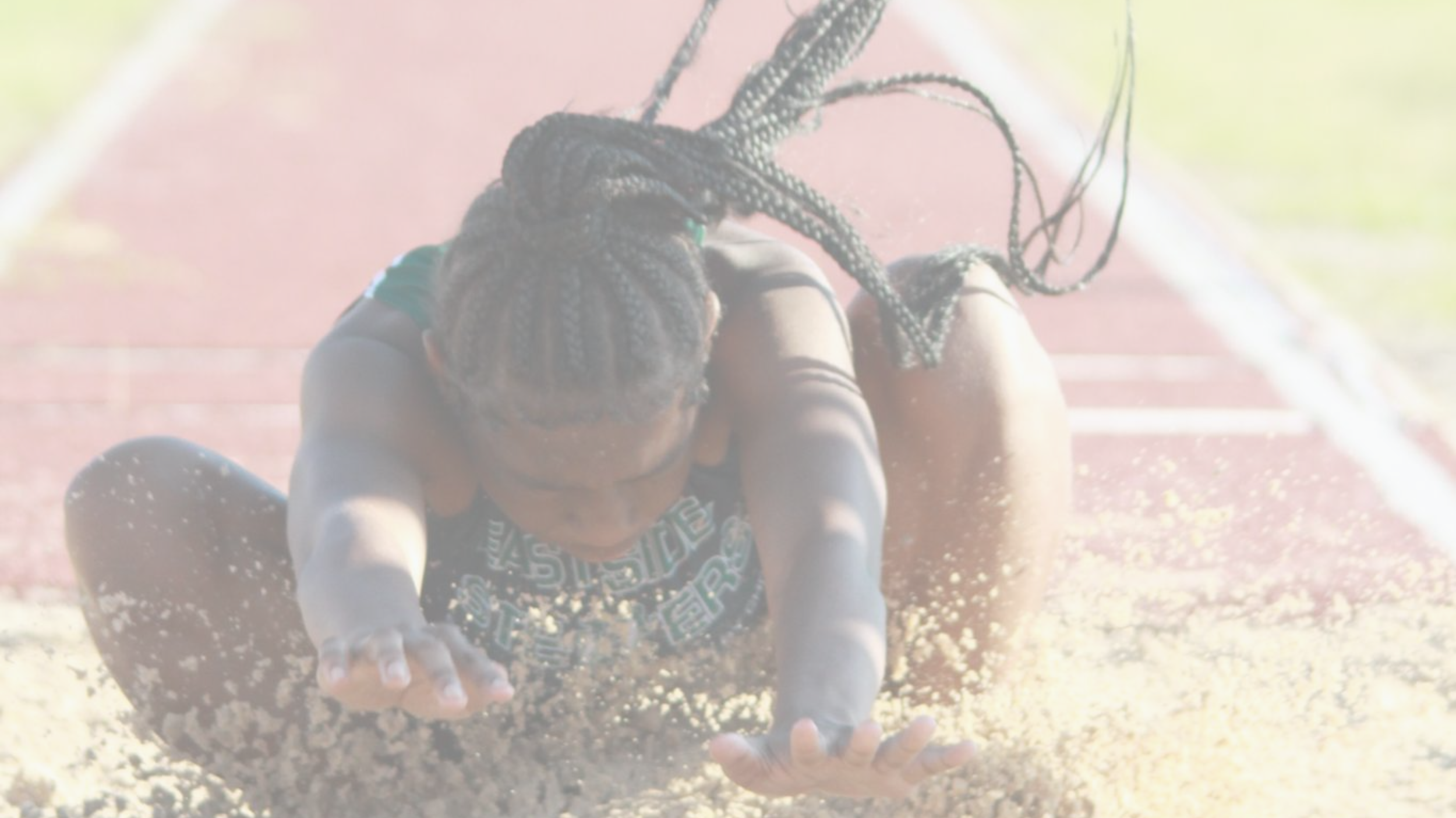 Athlete in a track and field event falling on the ground with sand spraying up around her.