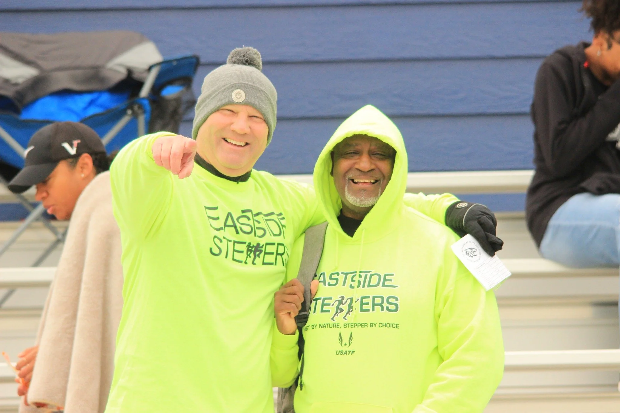 Two smiling men wearing bright yellow hoodies and one in a gray beanie, posing for a photo at an outdoor event.