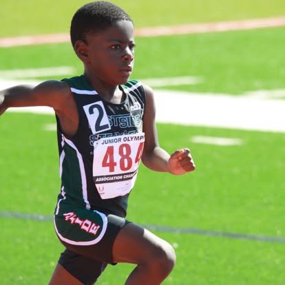 Young boy running in a track race wearing a black and green athletic uniform with the number 48.