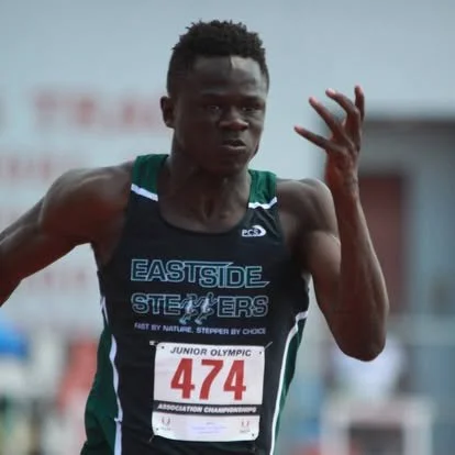 A male athlete running in a race, wearing a black and green uniform with the text 'EASTSIDE STEPPERS' and a bib number 474 in a track and field event.