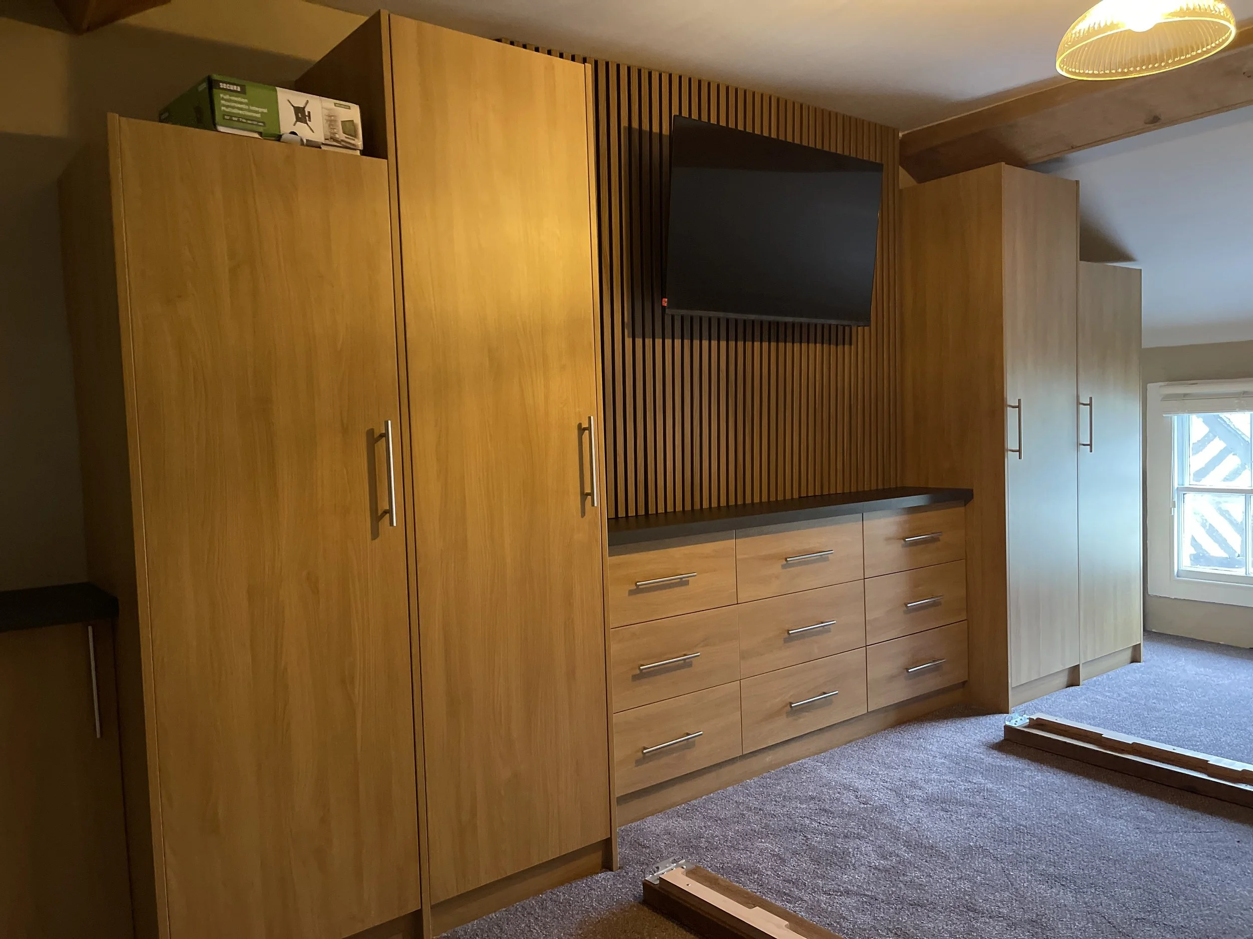 Room with wooden cabinets, a wall-mounted TV, a window, and a lamp on the ceiling.