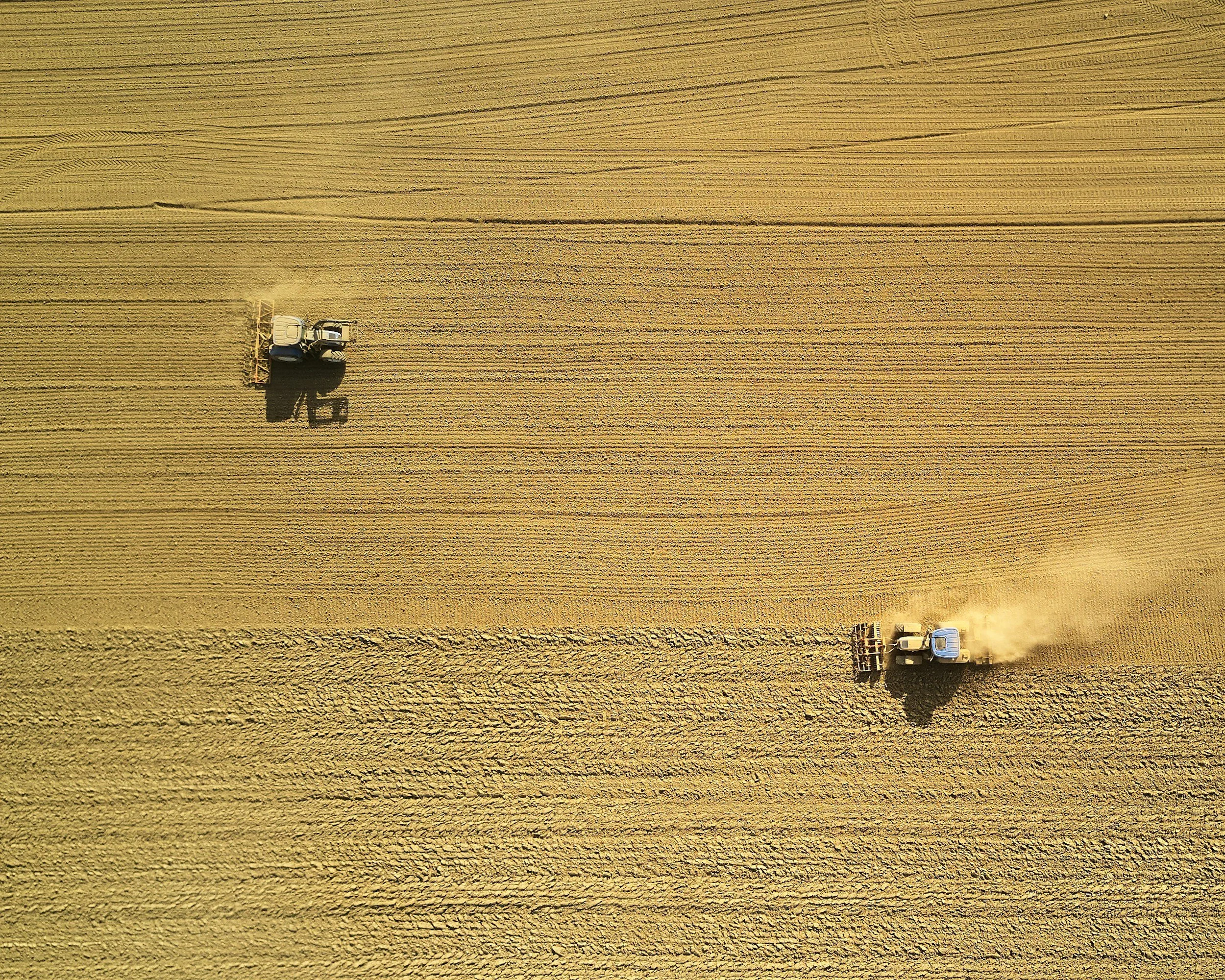 Two tractors working in a large golden wheat field, viewed from above.