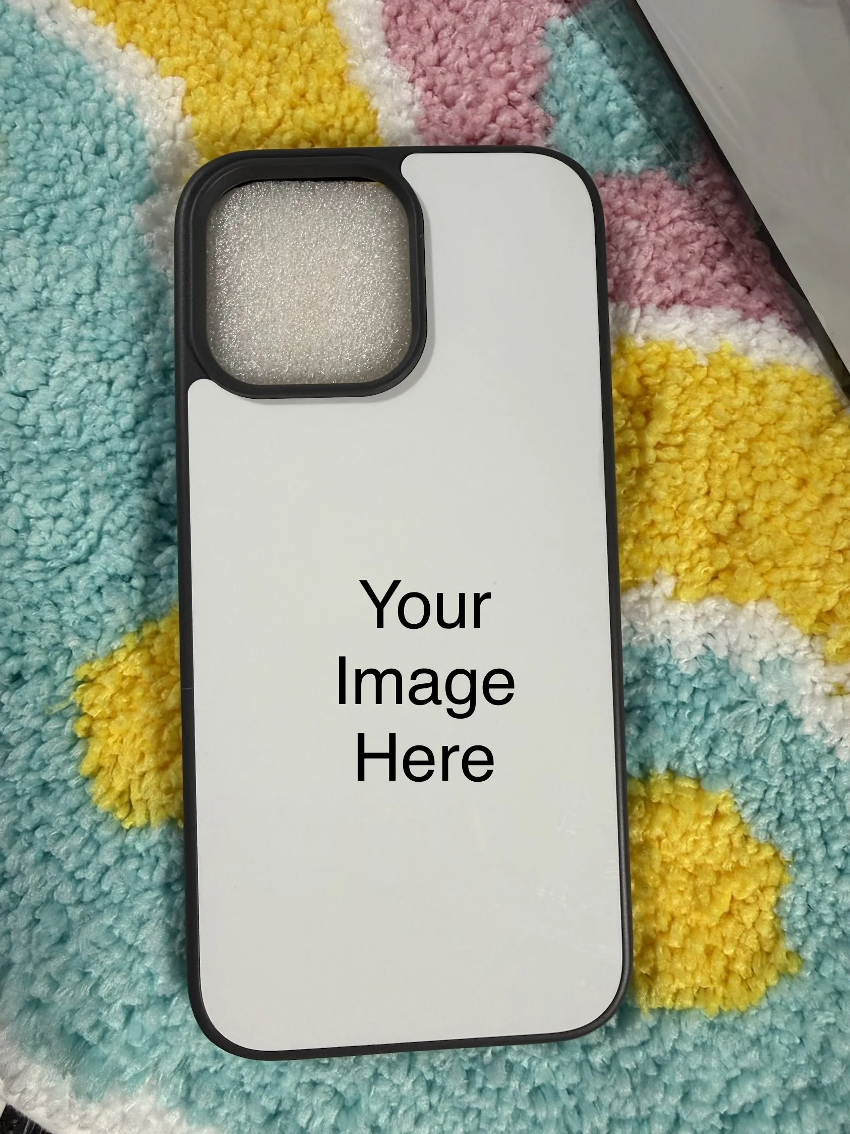 Close-up photo of a mobile phone case with a placeholder text 'Your Image Here' on a colorful plush blanket background.