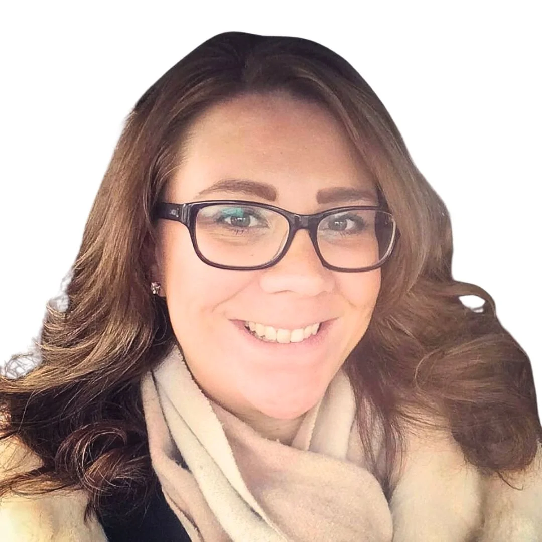 Smiling Scottish-Caucasian woman with long curly brown hair wearing thick black framed spectacles and coffee-coloured clothing. 