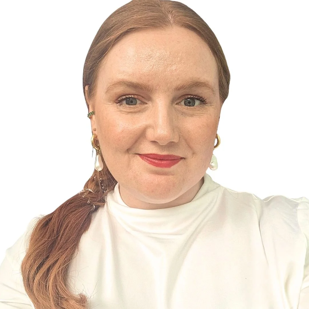 Smiling Scottish-Caucasian woman with red hair tied in a low ponytail style wearing a white turtleneck top