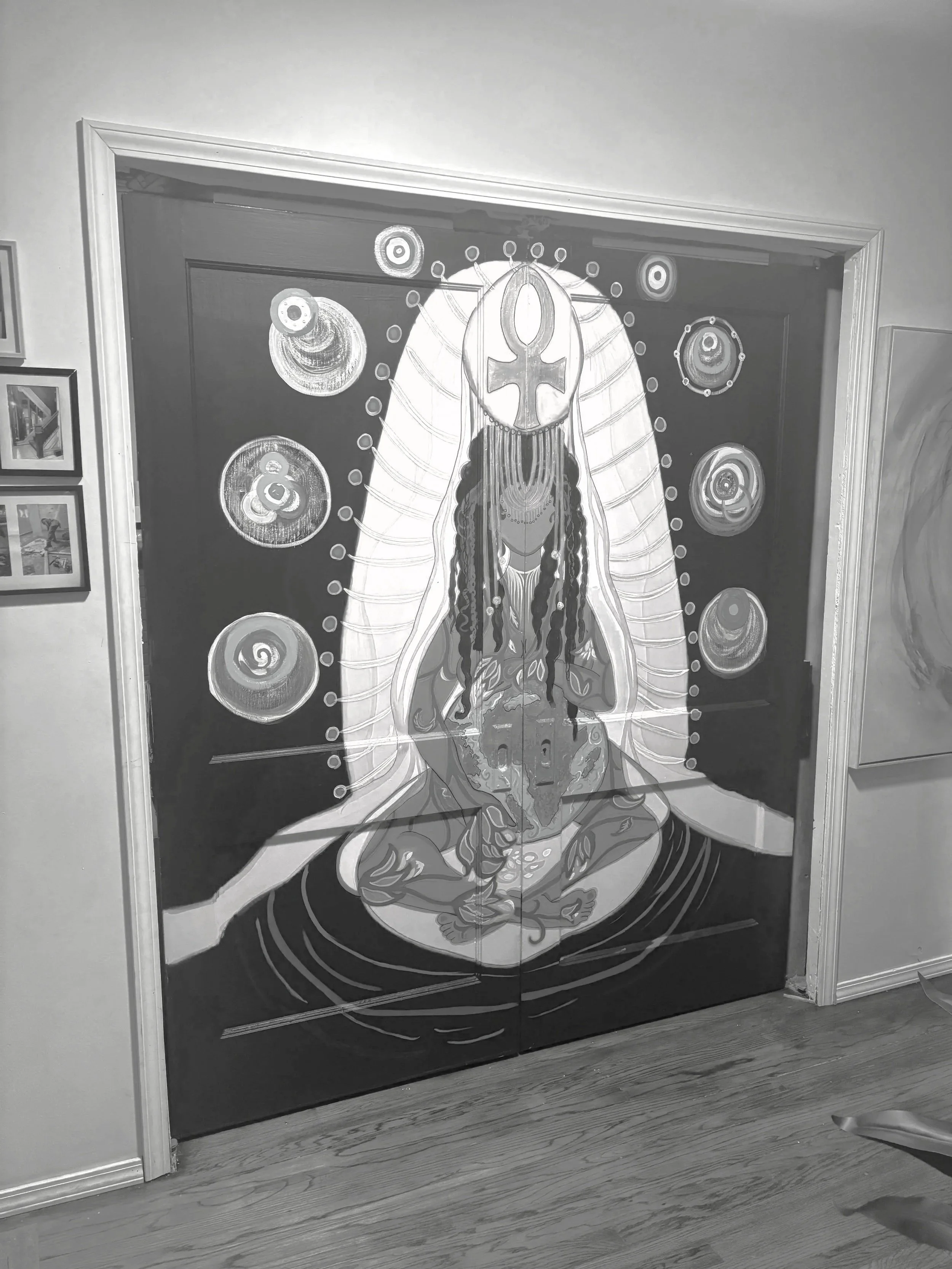 A black and white painting of a woman with long braided hair, seated in a meditative pose, with celestial symbols and circles surrounding her.