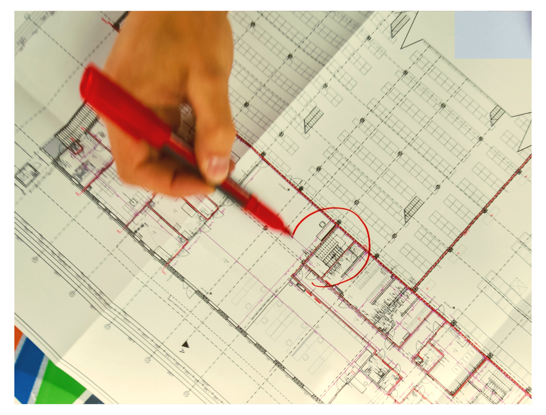 A person is marking or drawing on an architectural blueprint or floor plan with a red pen.