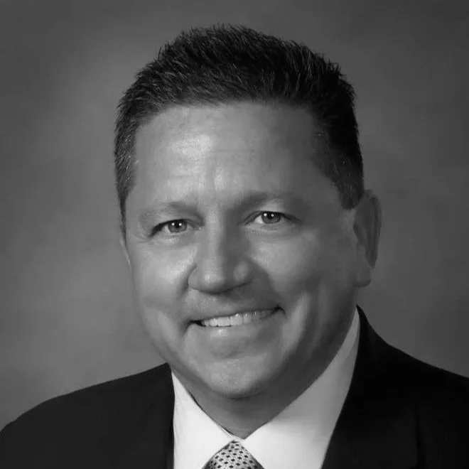 Black and white headshot of a smiling man wearing a suit and tie.