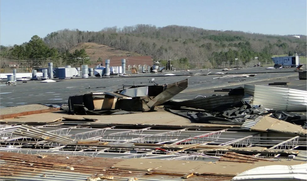 Debris and damaged roof materials after a storm or tornado, with a collapsed metal roof and scattered roofing panels on the ground.