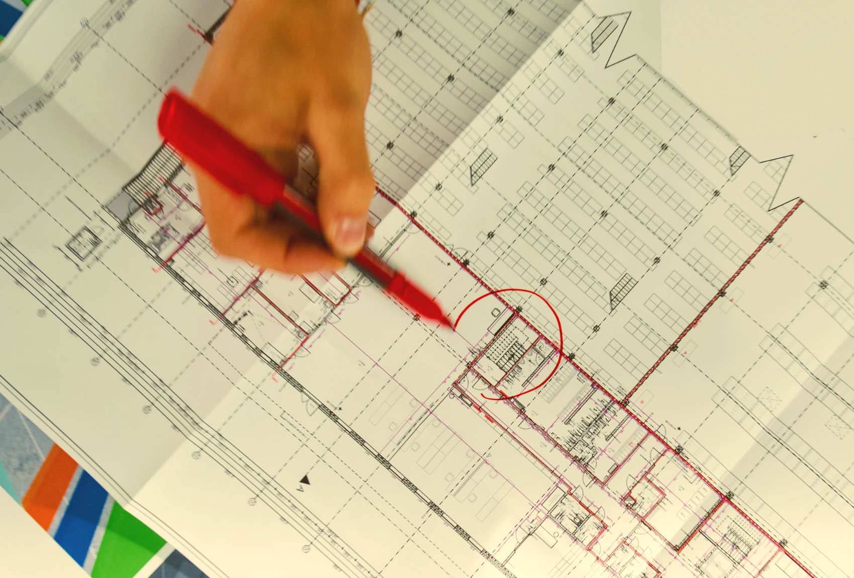 Person using a red marker to draw on an architectural blueprint.