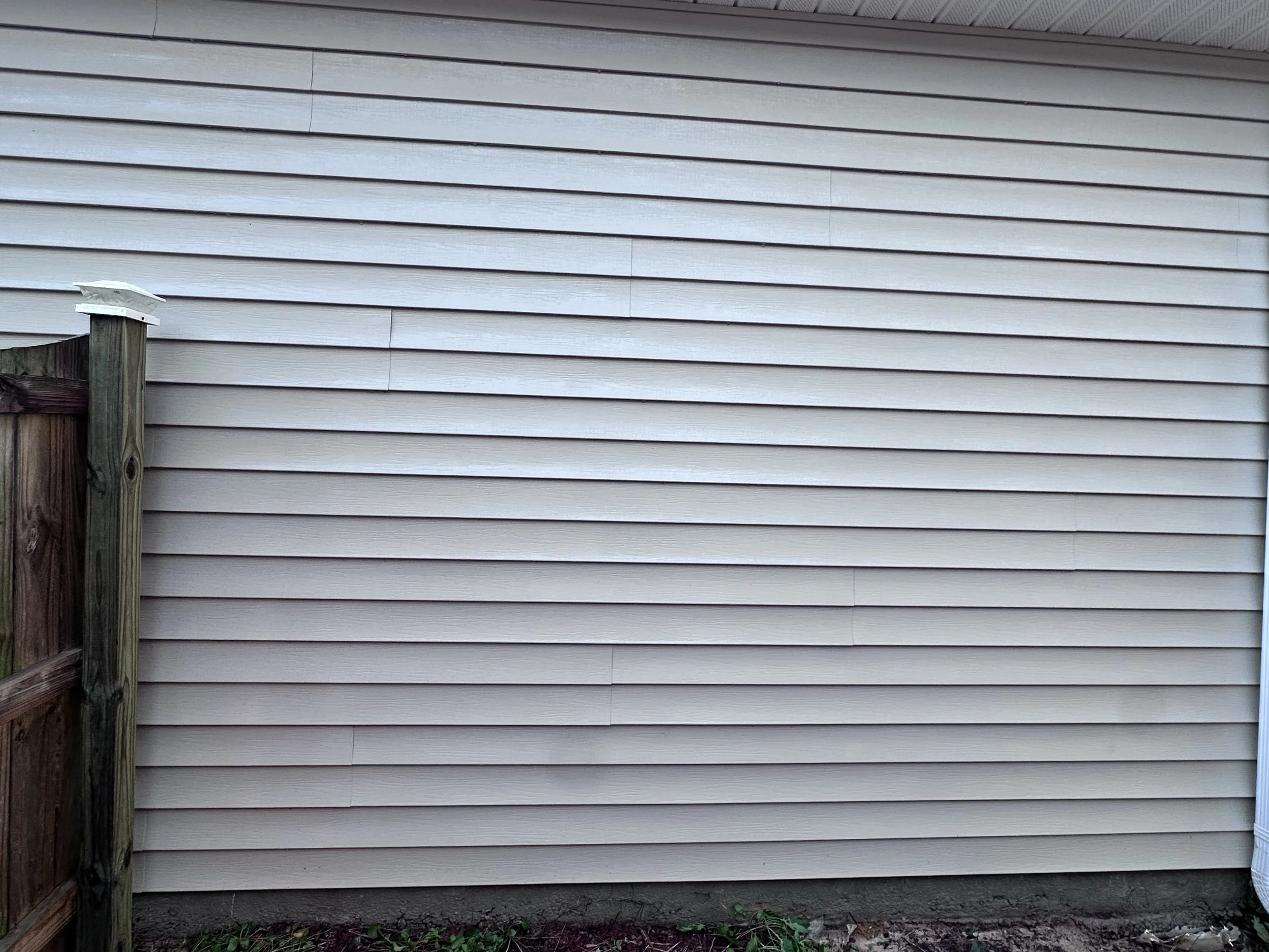 Exterior of a house with beige vinyl siding and a small section of a wooden fence on the left side.