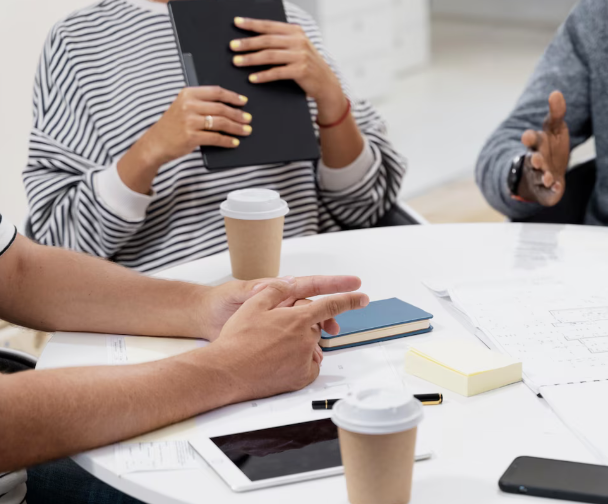 Groupe de personnes en réunion avec documents, table, tasses à café et appareils électroniques.