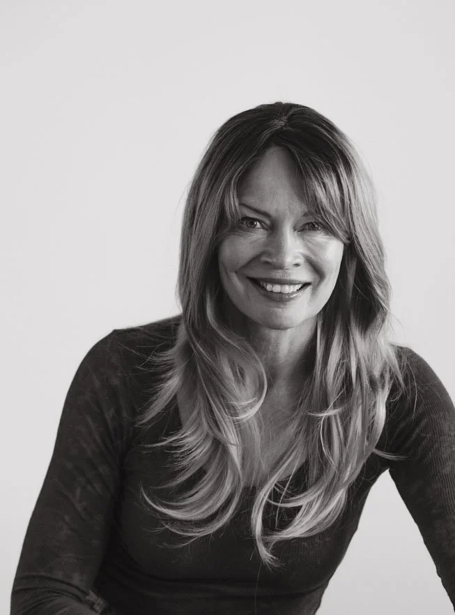 Black-and-white photo of a smiling woman with long, wavy hair, wearing a dark top.