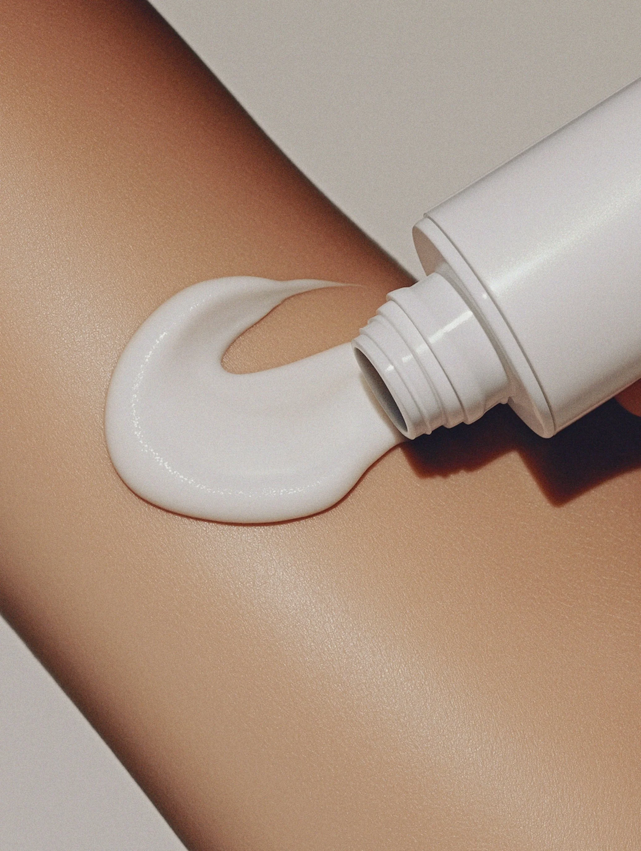 Close-up of white lotion being squeezed out of a tube onto a person's bare skin.