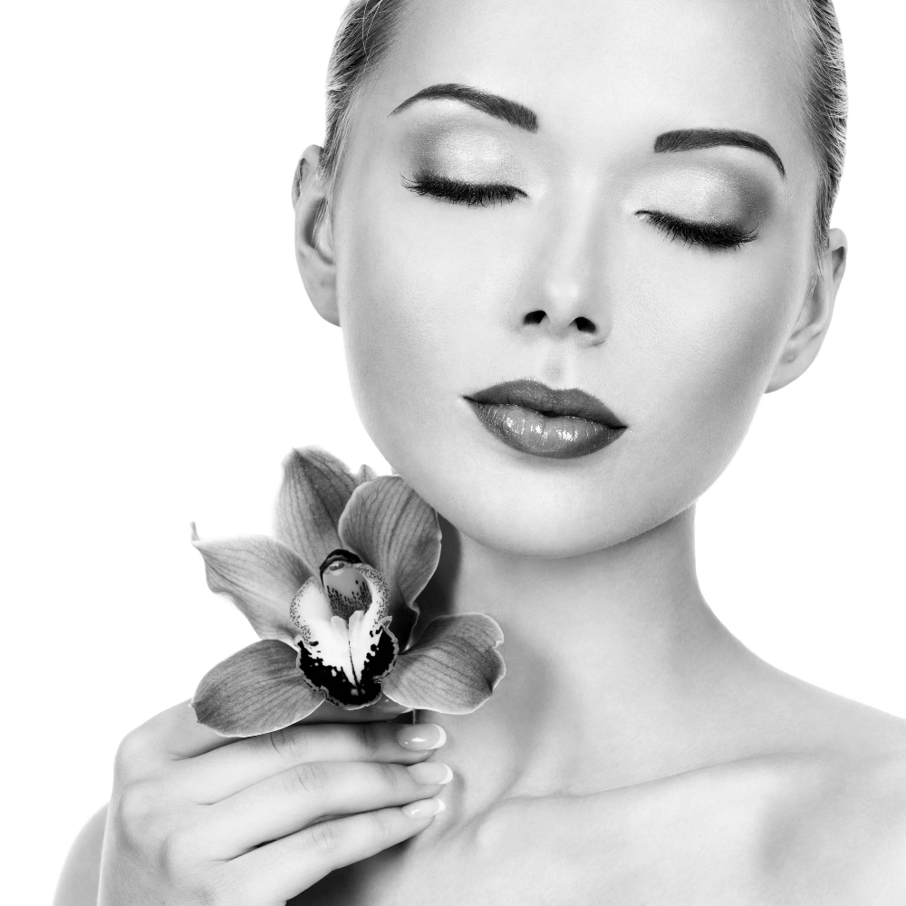 Black and white portrait of a woman with closed eyes, holding a flower near her shoulder.