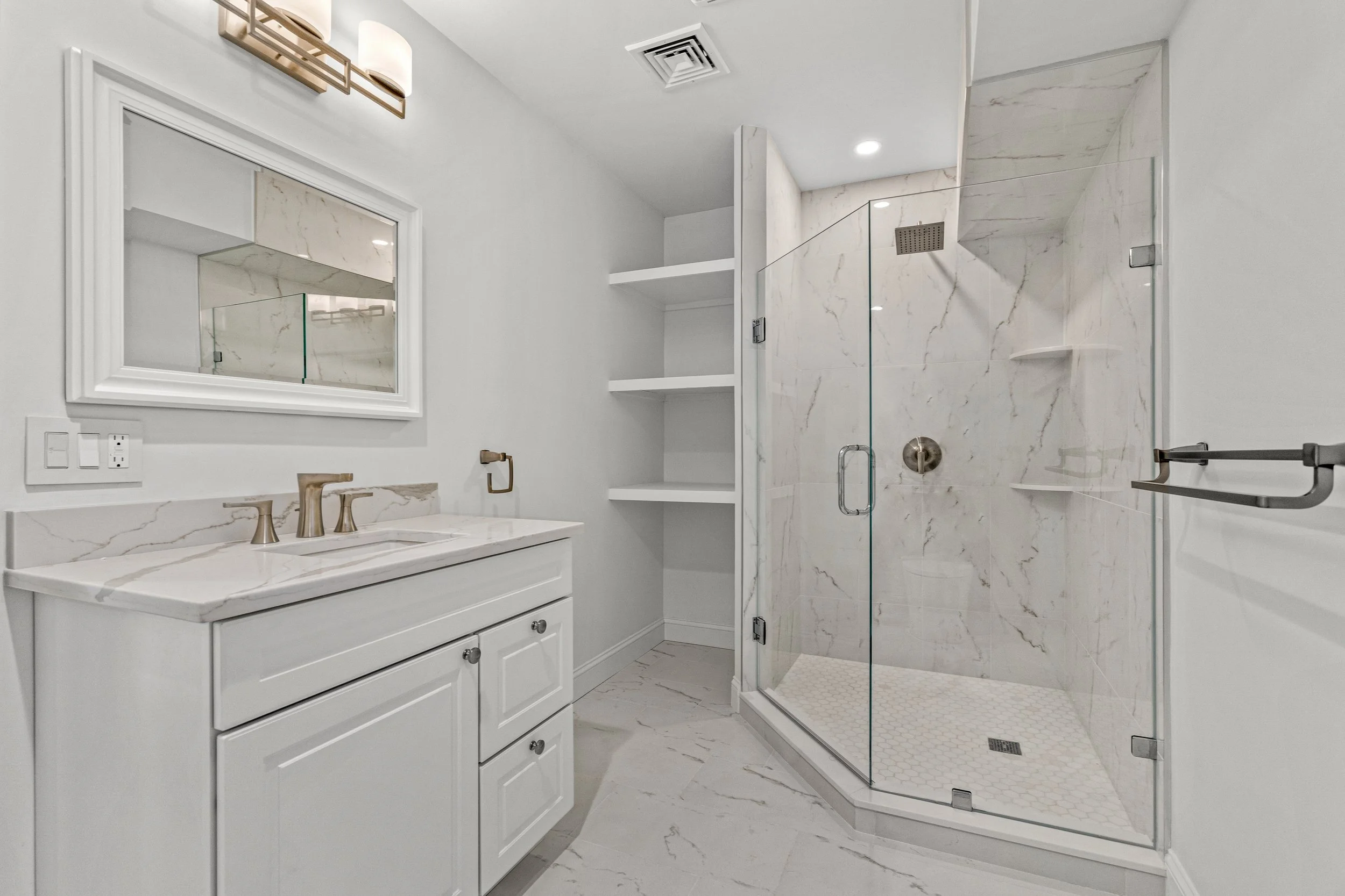 Modern white bathroom with a marble vanity, a large mirror, and a glass-enclosed shower with marble walls.