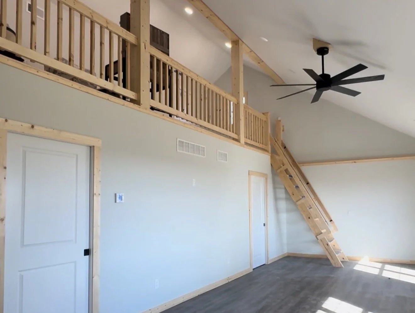 Interior of a room with a high ceiling, wood accents, a black ceiling fan, and a loft space accessible via a wooden ladder.