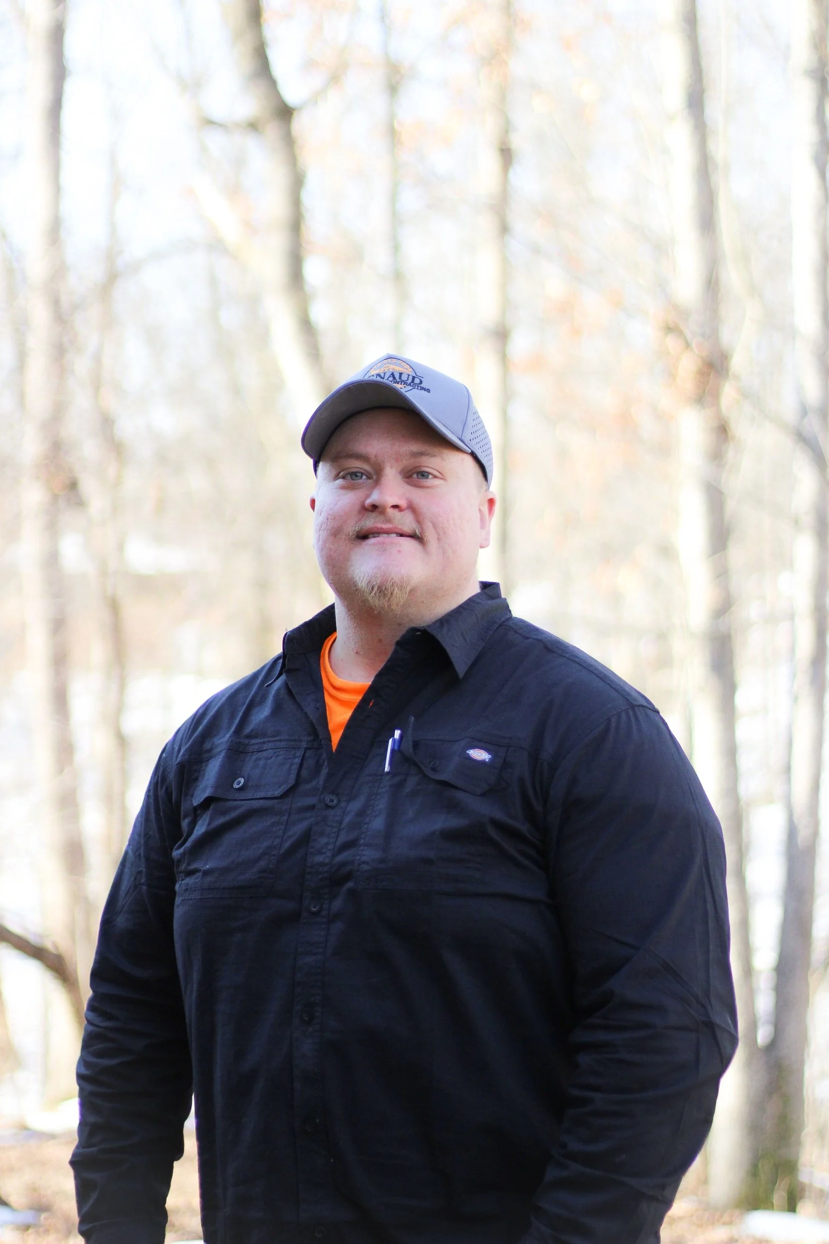 A young man sitting on a bench against a plain wall, wearing a grey polo shirt and beige pants, with a contemplative expression.