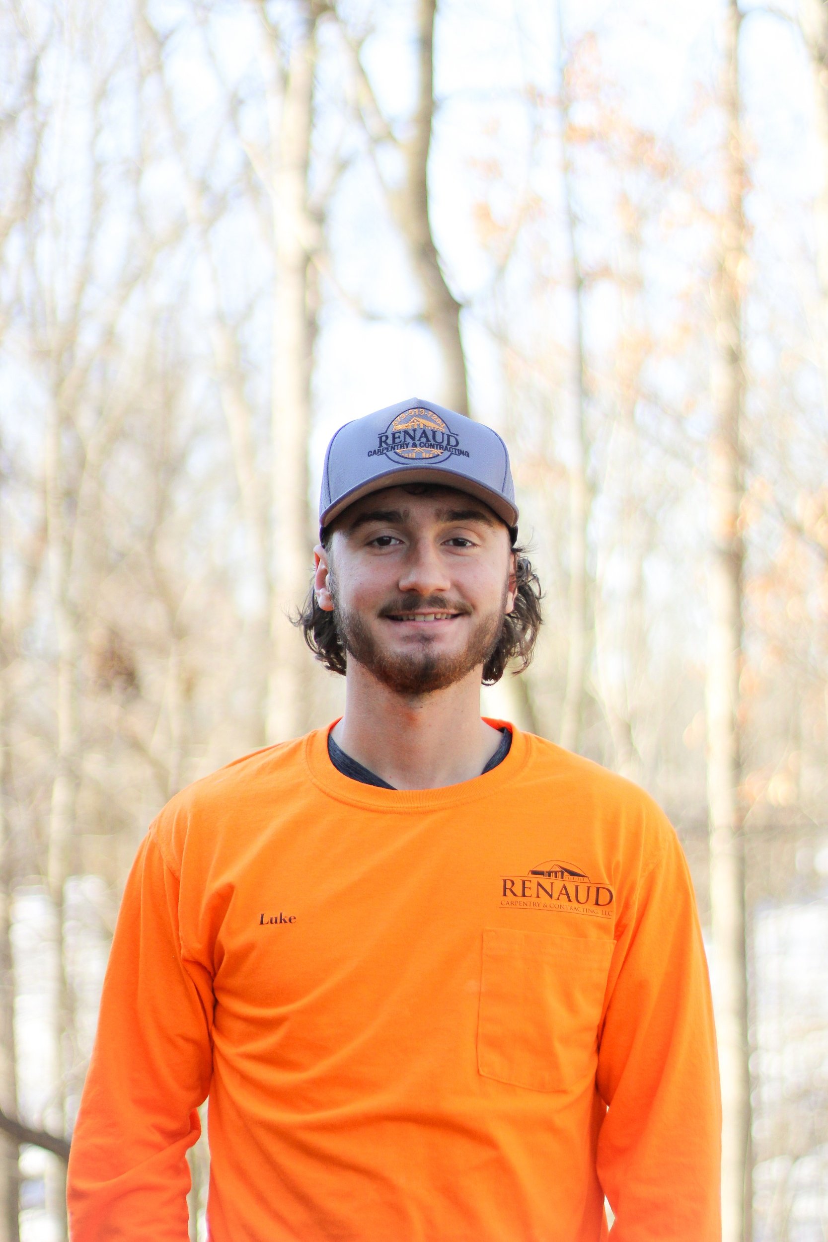 A woman with dark, wavy hair sitting on a white bench in a minimalist room, writing in a notebook, with abstract art leaning against a white wall behind her.