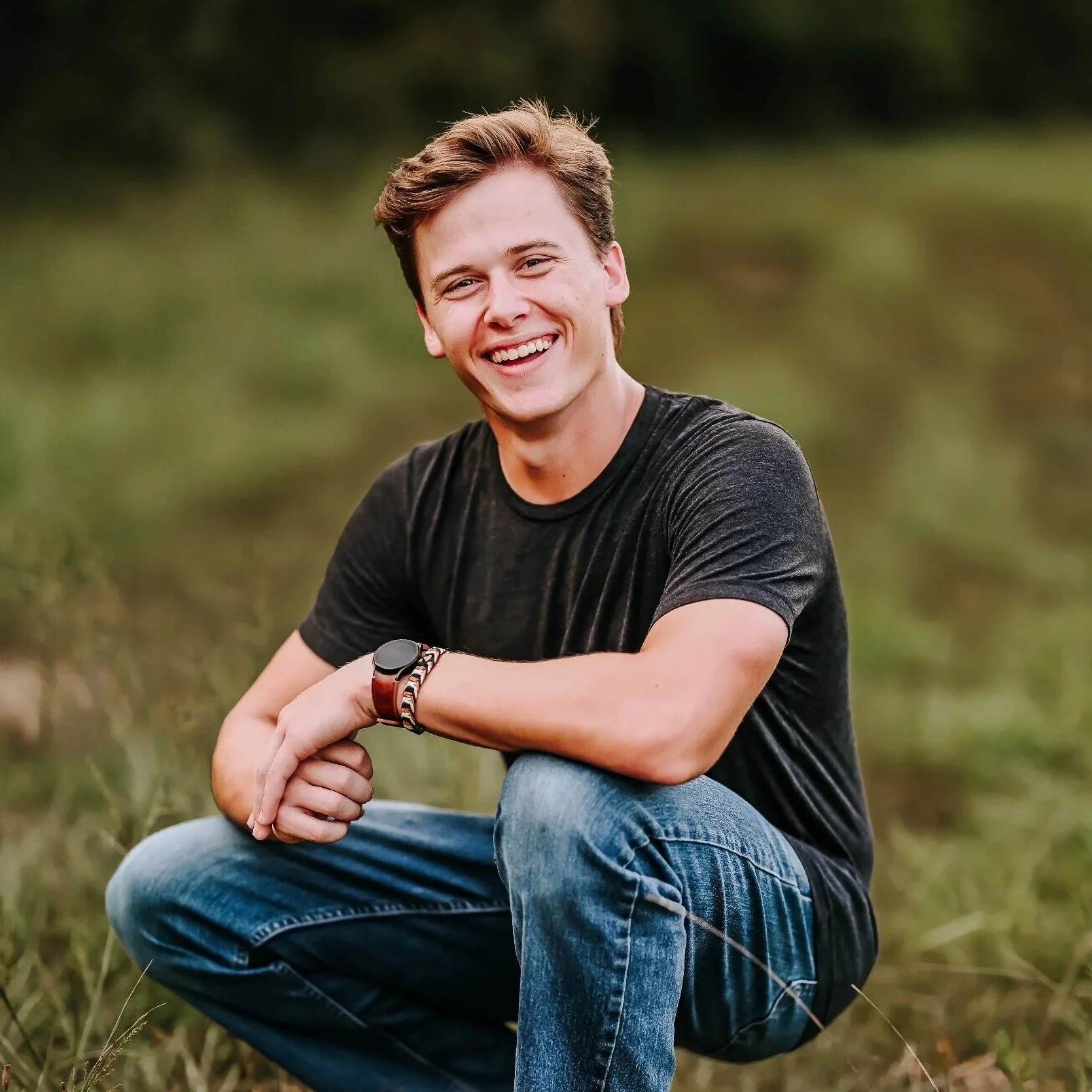 Young man taking a selfie on a construction site, giving a thumbs up and smiling, with two workers in the background installing roofing materials.