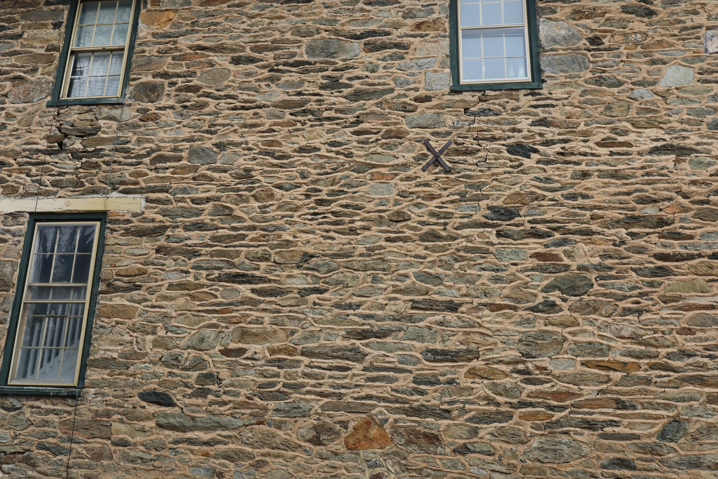 Close-up of a stone wall with two windows and a black X mark.