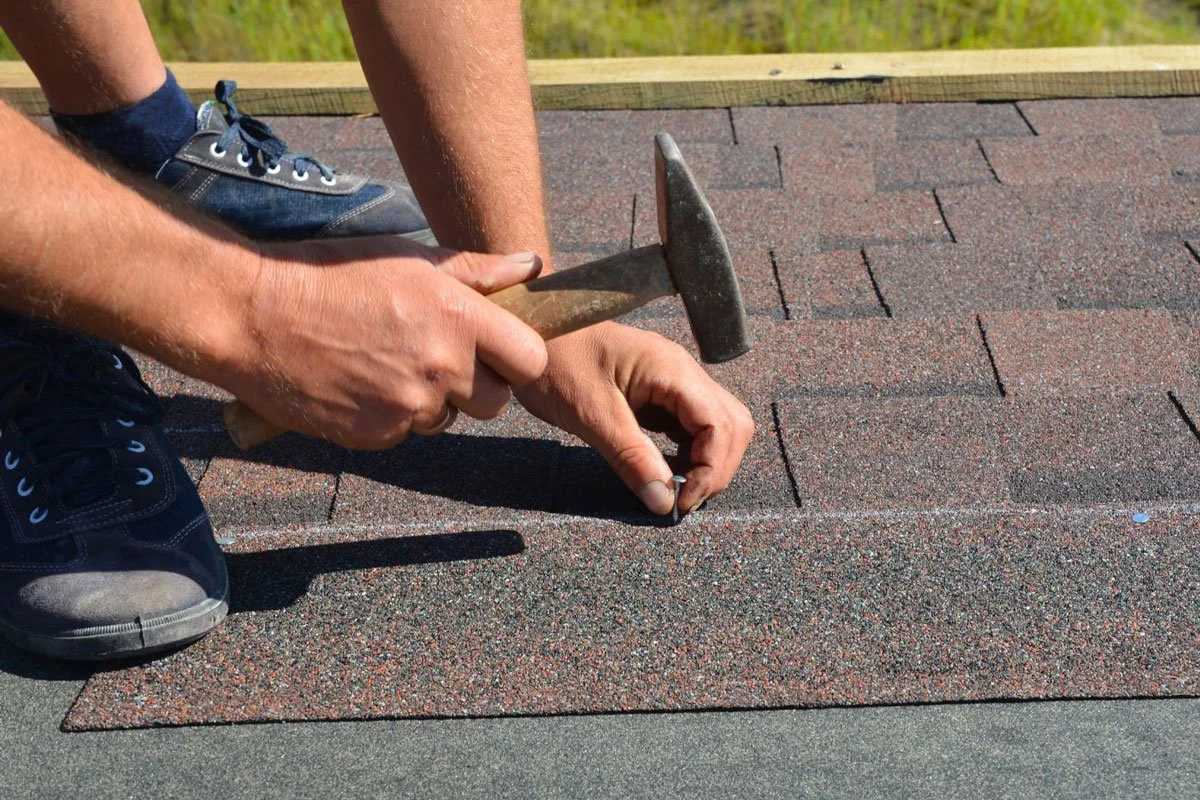 Person kneeling and installing asphalt shingles with a hammer