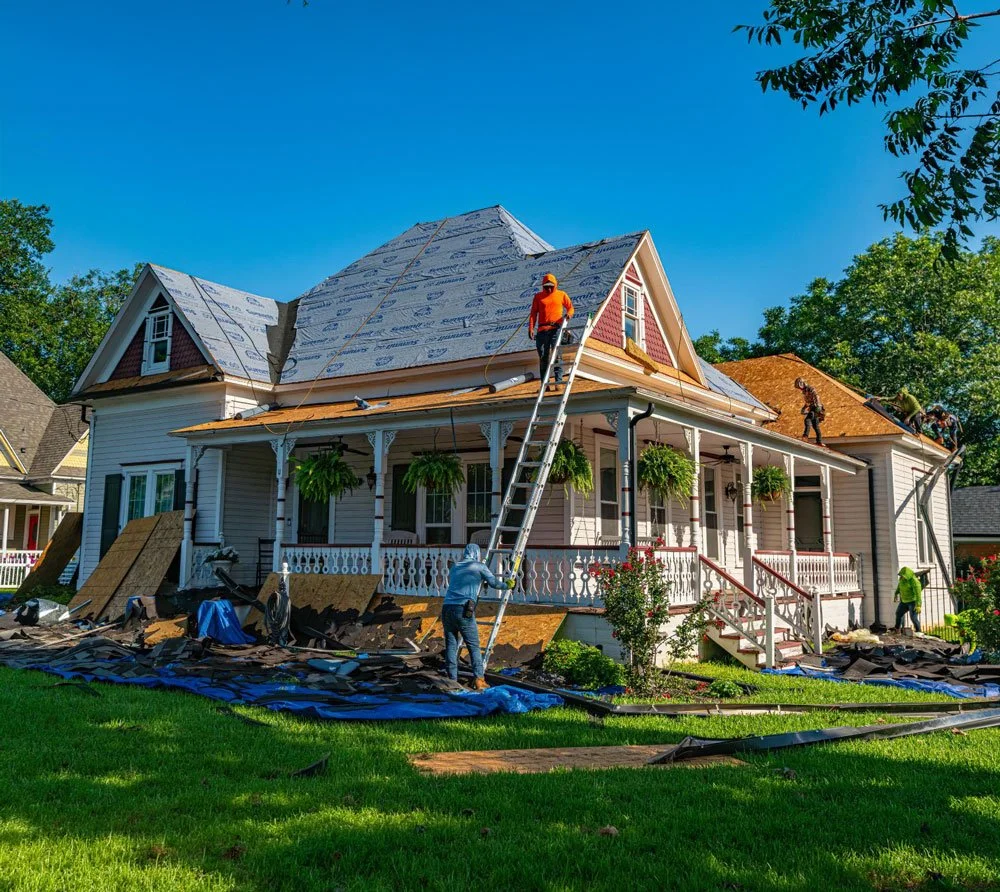 A house undergoing roof renovation with multiple workers installing new roofing materials on the roof on a sunny day.