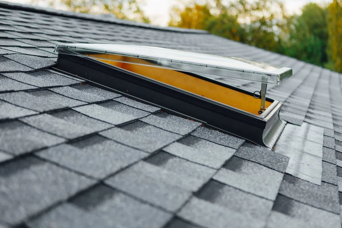 A solar tube skylight installed on a shingled roof, allowing natural light into the building below.