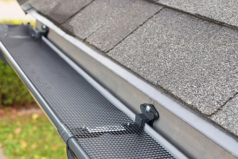 Close-up of a gutter guard installed along the edge of a house roof with grey shingles.