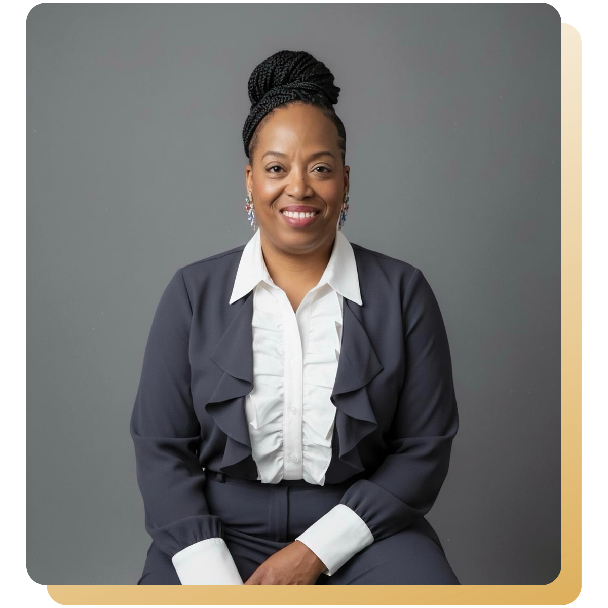Portrait of Geniece seated and smiling, wearing a navy suit and white blouse against a neutral background.