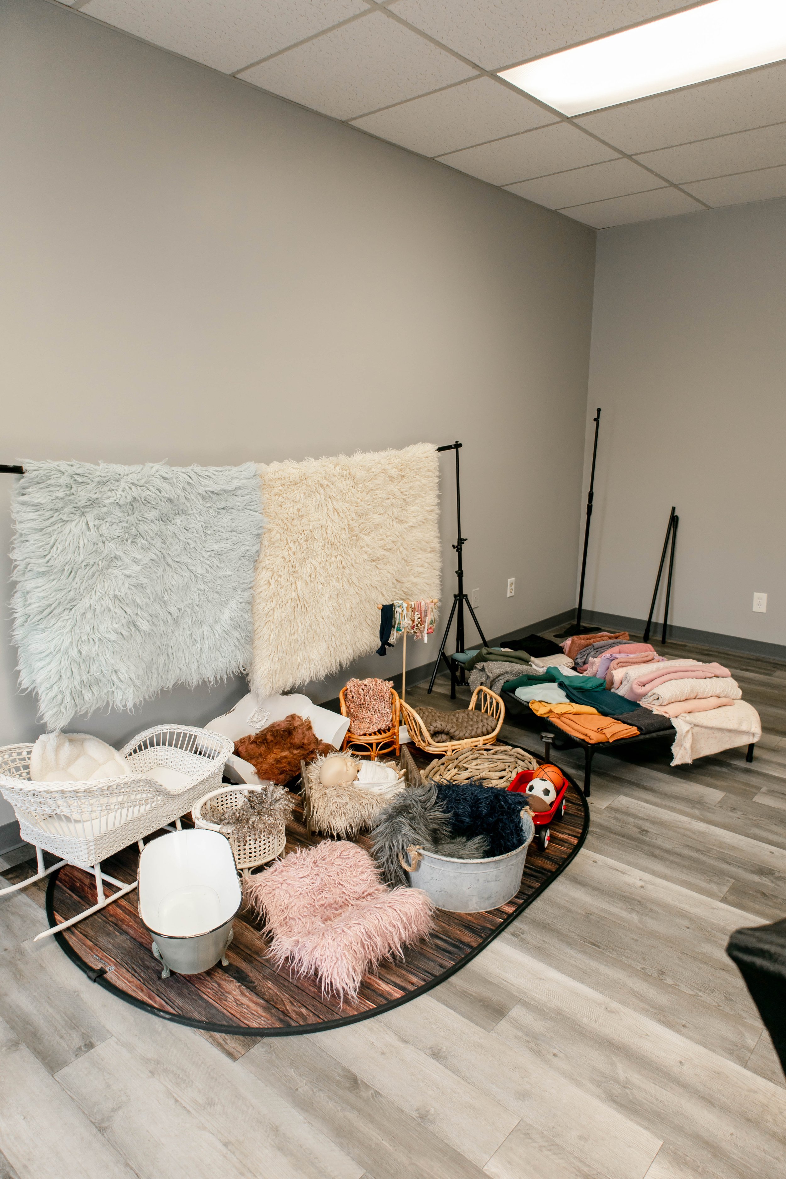 Room set up to show prop rental options for newbornphotoshoots with fluffy blankets, rugs, and stuffed animals, with lighting equipment and clothing racks in the background.