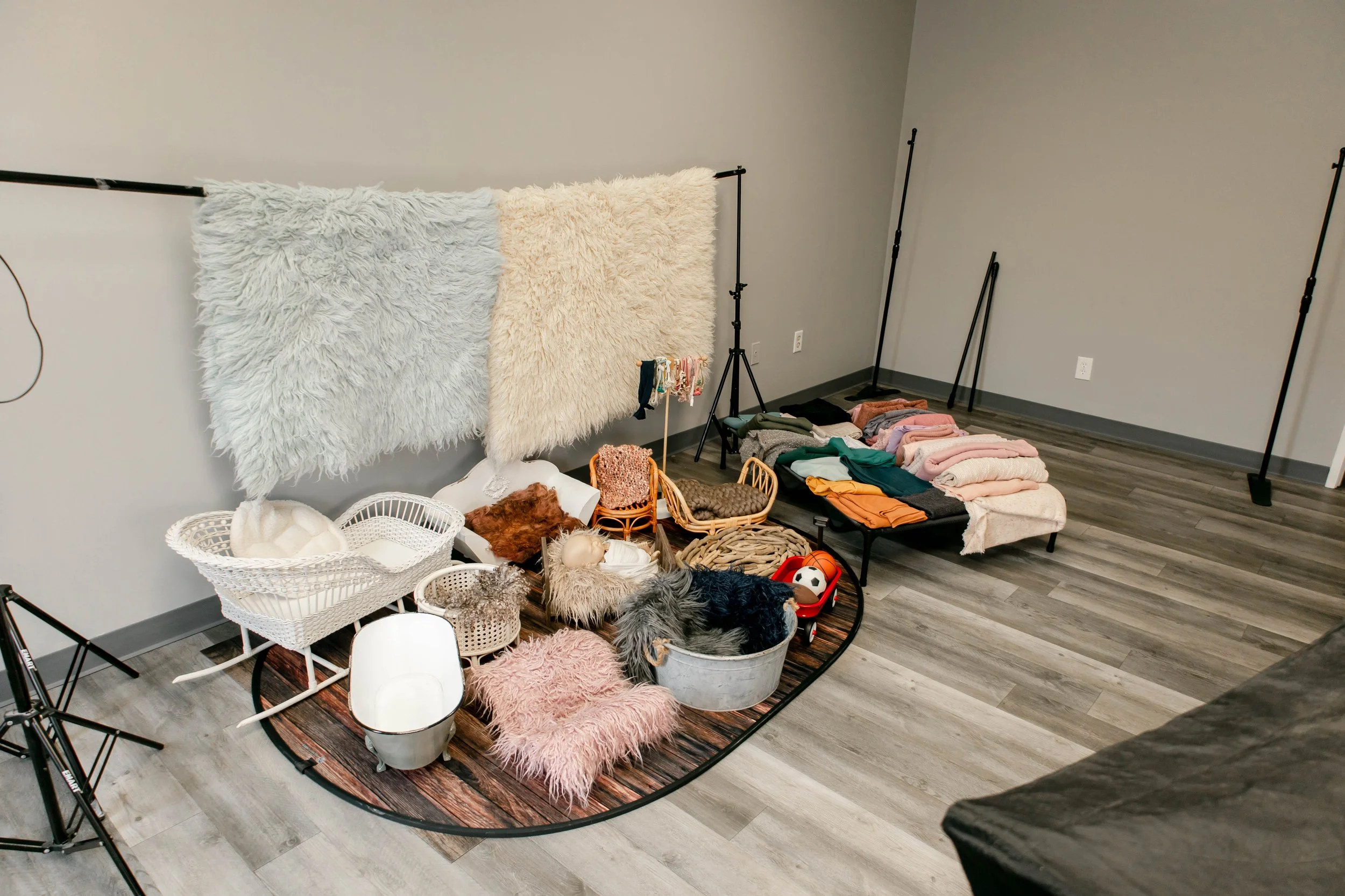 A photography studio setup with drapes and various props, including baskets, rugs, and pet toys, arranged on a wooden floor near a gray wall.