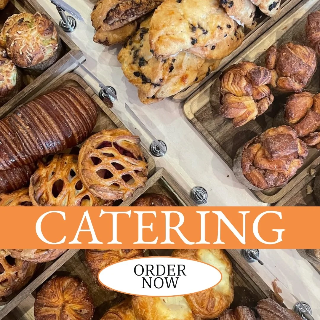Various baked goods including croissants, muffins, danishes, and bread displayed in wooden trays, with an overlay text that reads "Catering" and a button labeled "Order Now."