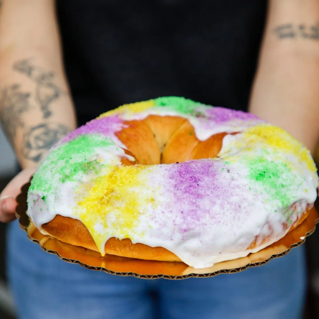 A person holding a colorful donut with white icing and rainbow sprinkles around the top edge.