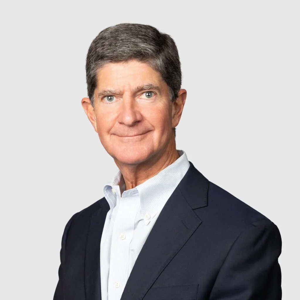 A man with gray hair in a suit against a light gray background.