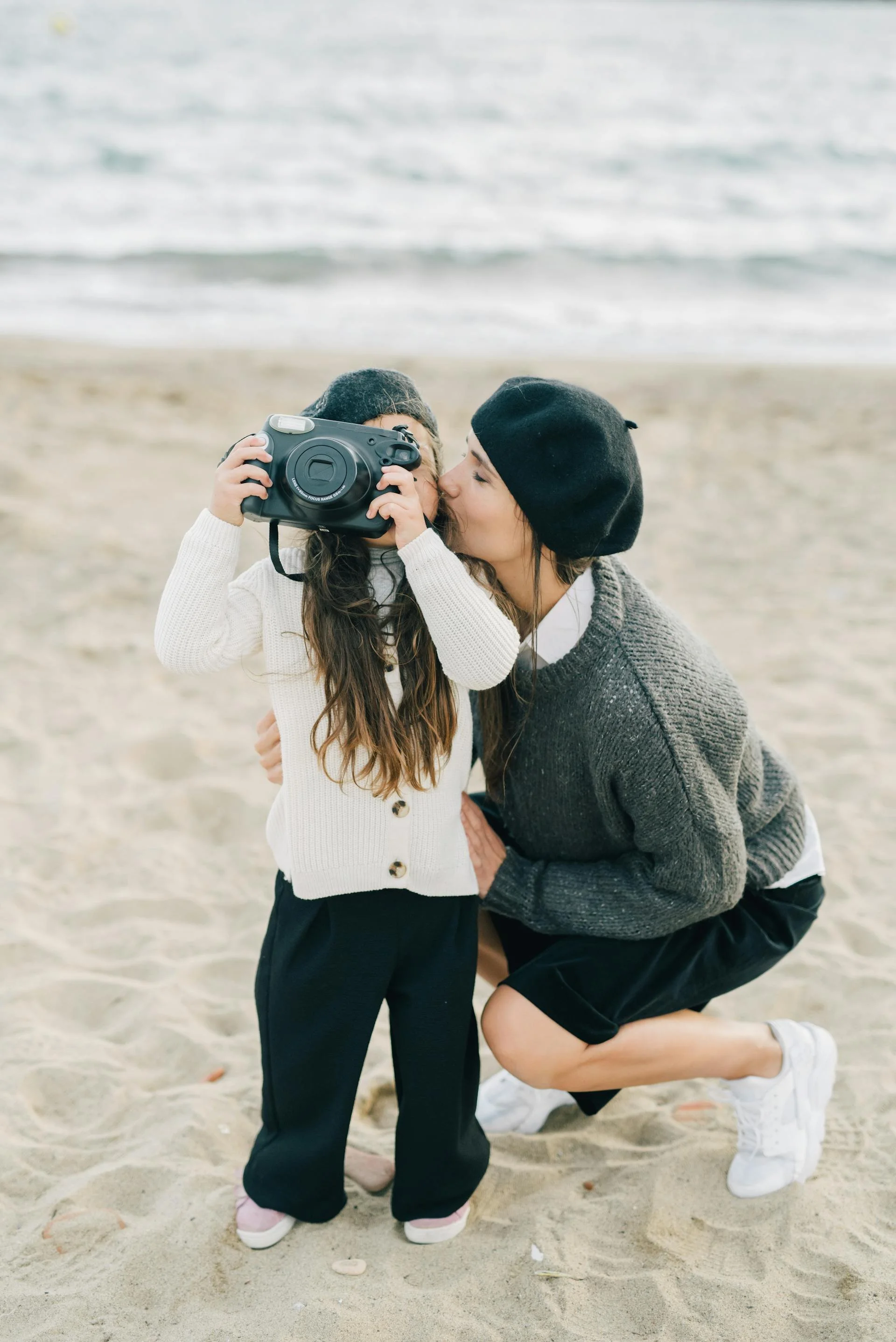 Une femme et une jeune fille à la plage, la femme fait un bisou à la fille qui regarde à travers un appareil photo.