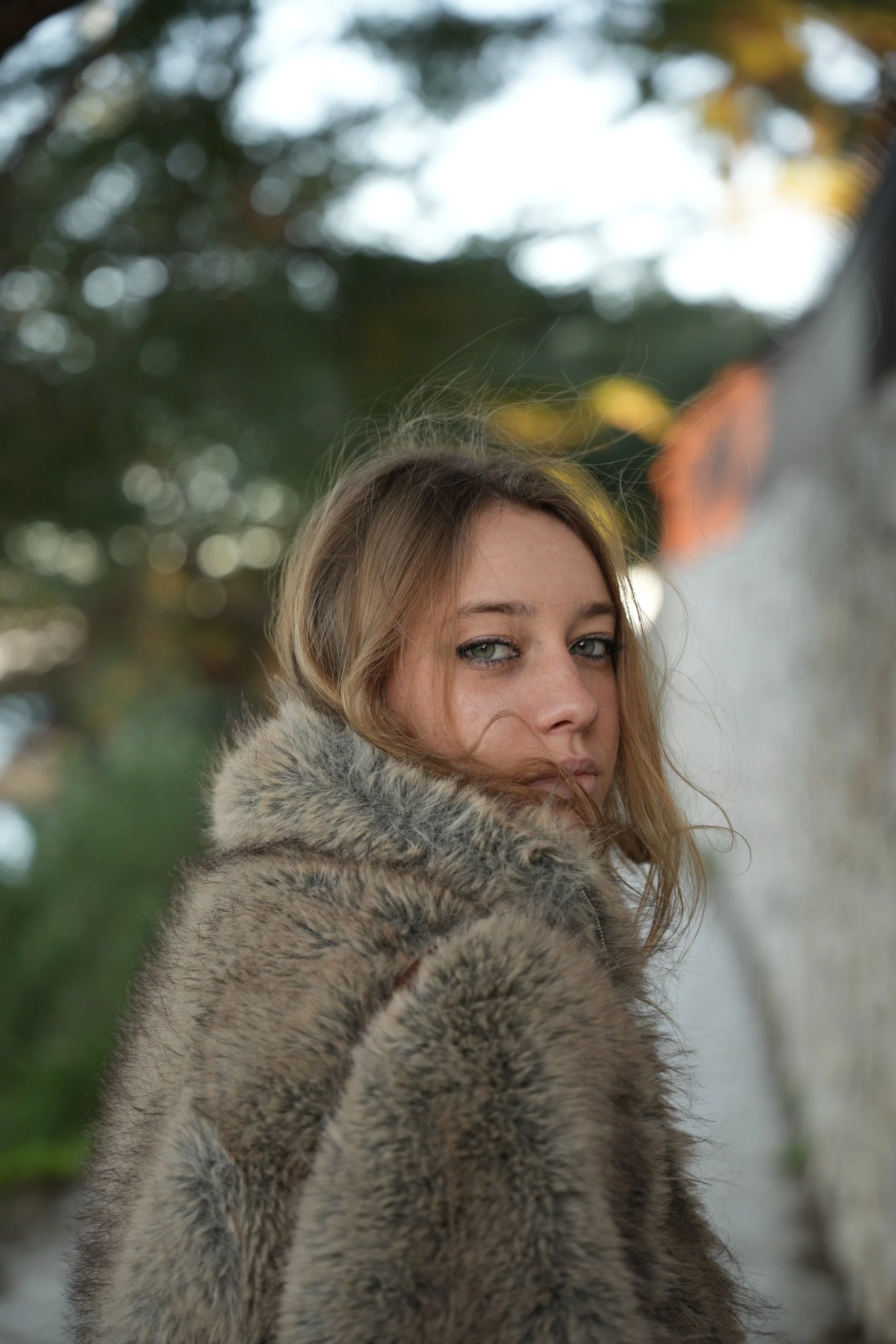 Jeune femme avec des yeux verts portant un manteau en fourrure, regardant par-dessus son épaule.